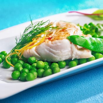 Grilled or oven baked fish fillet topped with lemon zest and served on a plate with peas, mangetout or sugarsnap pea, and fresh dill for a healthy seafood diet