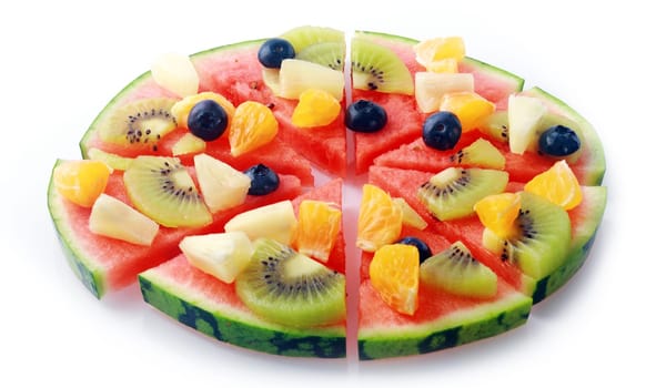 Tropical fruit pizza on a watermelon base topped with pineapple, orange, kiwifruit and blueberries cut into segments on a white background for healthy vegetarian cuisine