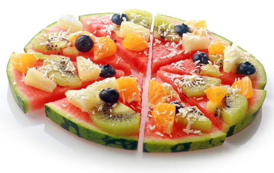 Low angle close up view of a sliced exotic tropical fruit watermelon pizza topped with kiwifruit, blueberries, orange, pineapple, and sprinkled with desiccated coconut for a fun dessert at a party
