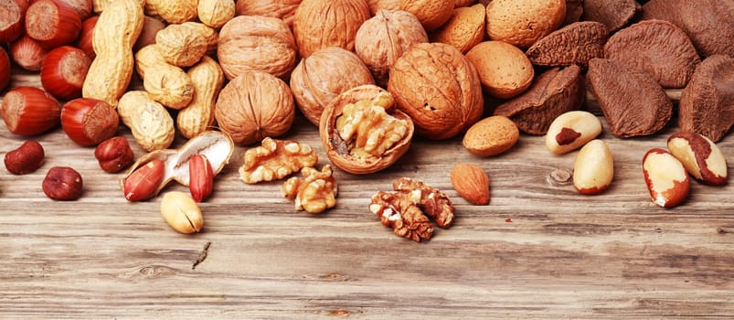 Variety of shelled and whole nuts in a horizontal banner including almonds, hazelnuts, brazil nuts, peanuts and walnuts on a rustic wooden background with copyspace