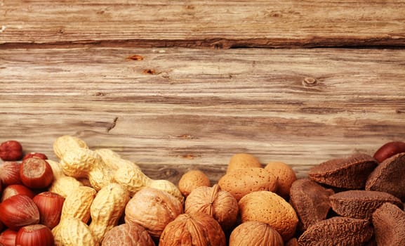 Border of assorted whole nuts in their shells including almonds, hazelnuts, brazil nuts, peanuts and walnuts on textured rustic wood with copyspace