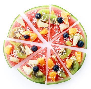 Colorful tropical fruit watermelon pizza topped with kiwifruit, blueberries, orange, pineapple, and sprinkled with desiccated coconut, cut into segments for serving, on white overhead view