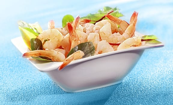 Bowl of delicious grilled prawn or shrimp tails garnished with fresh lemon and baby spinach on a colorful turquoise blue background