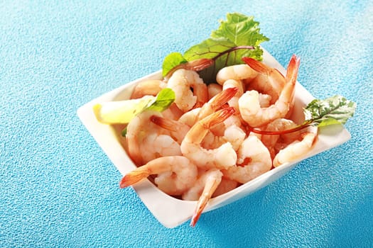 Gourmet pink prawn or shrimp tails served in a dish with lemon and fresh herbs for a delicious seafood appetizer to a dinner, high angle view on turquoise blue with copyspace
