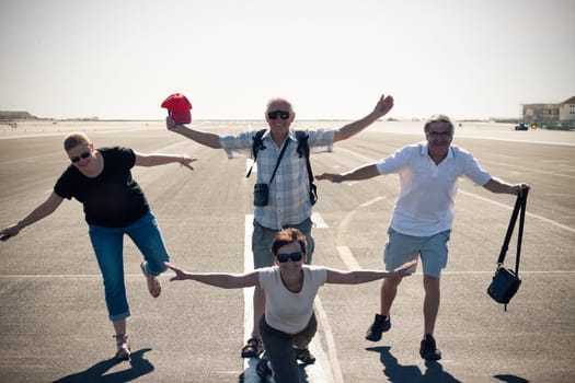 Funny group of tourist people imitating airplane at the airport runway.