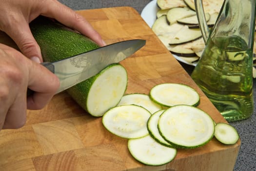 Woman's hand is slicing the zucchini on a wooden board.