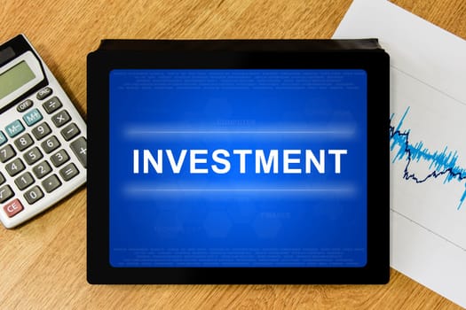 financial investment word on digital tablet with calculator and financial graph