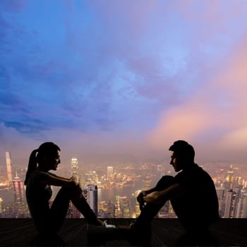 Silhouette of young couple face to face sit on ground in the city night.