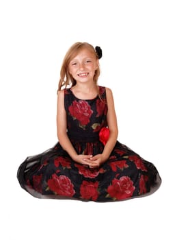 A beautiful little girl in a black and red dress sitting smiling on the floor,.isolated on white background..