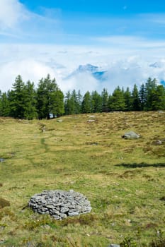 Cloudy L'Arpille Mountain seen from La Giete, in Switzerland, with pine trees and rocks in the foreground.