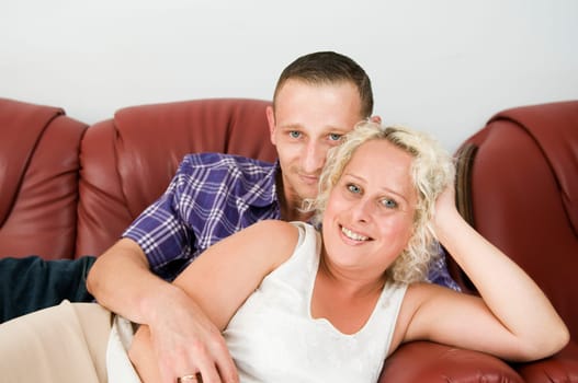 Torso portrait of a young couple lying on a brown leather sofa and happily smiling into the camera