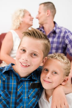 Head-and-shoulder portraits of two brothers,aged 7 and 13,with their fuzzy parents sitting on a sofa in the background,looking at each other