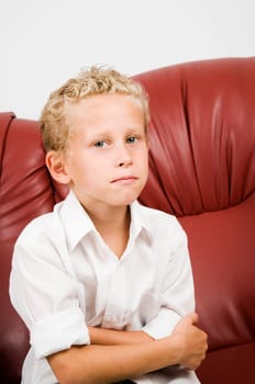 Upper body portrait one seven year old blonde curly boy on brown leather sofa against white background