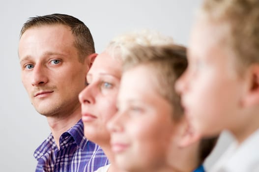 Head portrait of a young father with a wife lined up next to him and two sons. The focus is on father.