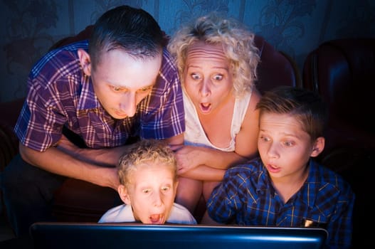 Parents with their two sons,aged 7 and 13,sitting on the couch in a darkened room and looking at the camera in shock at a monitor