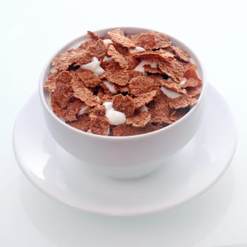 Bowl of crispy flakes of chocolate flavored breakfast cereal in milk for a tasty nutritional meal served in a white ceramic bowl and saucer , in square format