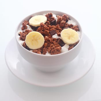 Delicious bowl of crunchy chocolate breakfast cereal with sliced fresh tropical banana and choc chips of dark chocolate , high angle square format
