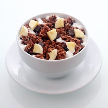 Bowl of tasty flavored chocolate breakfast cereal with diced fresh banana and chips of dark chocolate candy in a crunchy roasted muesli