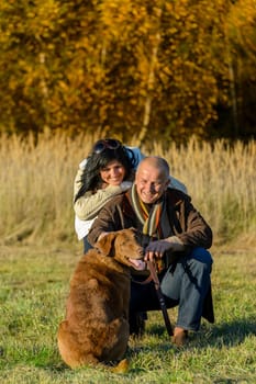 Cheerful couple with retriever dog in autumn countryside sunset