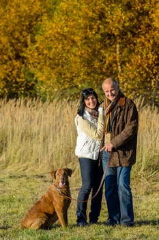 Cheerful couple with dog in park autumn sunset