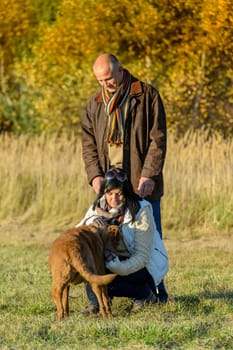 Mature couple playing with retriever dog autumn sunny park