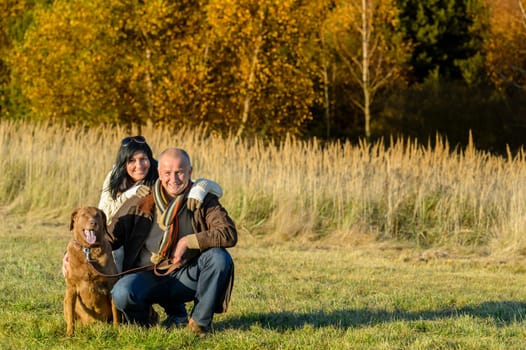Cheerful couple with retriever dog in autumn countryside sunset