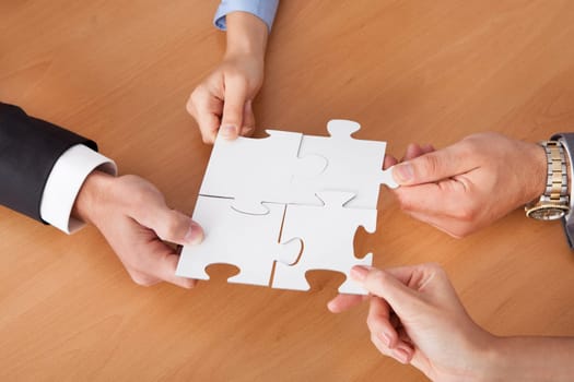 Close-up Of Businesspeople Holding Jigsaw Puzzle Over Desk