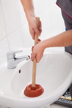 Portrait of male plumber pressing plunger in sink