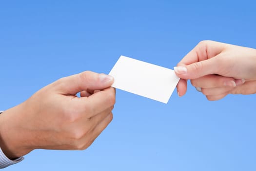 Close-up Of Hand Exchanging Visiting Card Over Blue Background
