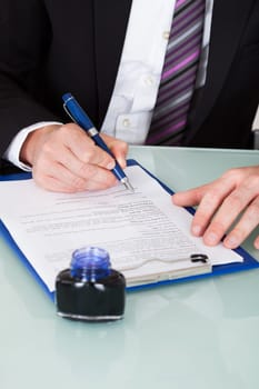 Close-up Of Businessman Hand Writing With Ink Pen Over Document