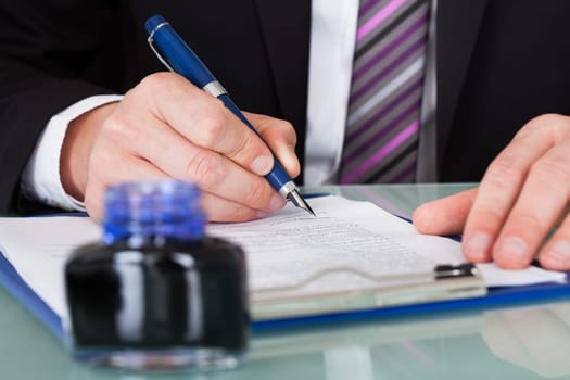 Close-up Of Businessman Hand Writing With Ink Pen Over Document