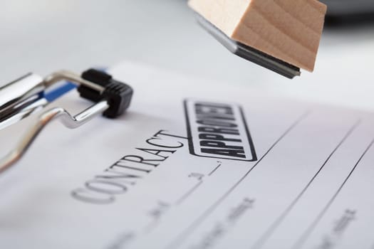 Close-up Of Business Man Hand Pressing Rubber Stamp On Document