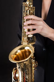 Beautiful young woman playing saxophone over black background