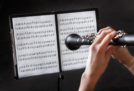 Beautiful young woman playing clarinet over black background