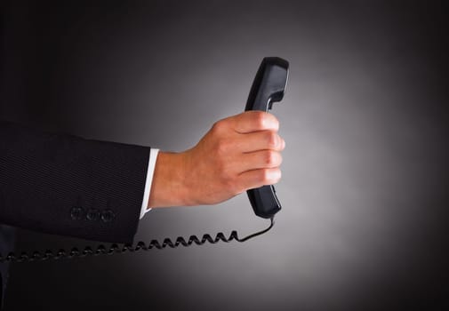 Close-up Of Hand Holding Telephone Receiver Over Black Background