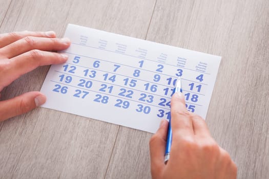 Close-up Of Man Marking With Pen And Looking At Date On Calendar