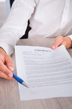 Businessman's Hand Holding Pen And Contract Paper On Desk