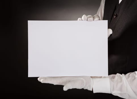 Closeup Of Young Waiter Presenting Blank Placard Over Black Background