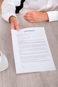 Businessman's Hand Holding Contract Paper On Desk
