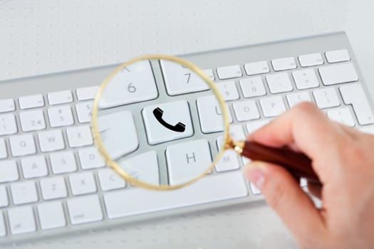 Close-up of hand looking at phone key through magnifying glass
