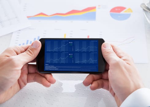 Businessman Analyzing Graph On Cell Phone In Office