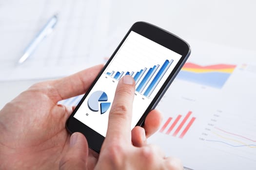 Businessman Analyzing Graph On Cell Phone In Office
