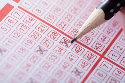 Close-up Of A Person Marking Number On Lottery Ticket With Pencil