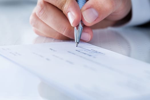 A Male Hand Filling Out The Amount On A Cheque