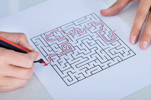 Close-up Of Hand Solving Maze Puzzle With Red Pen