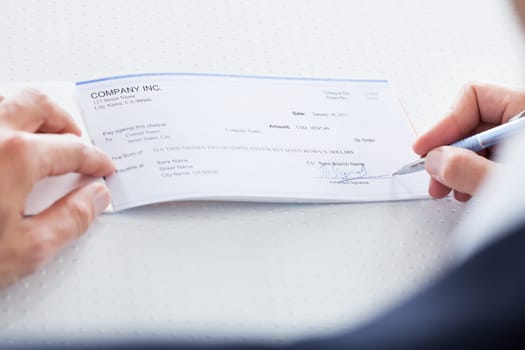 A Male Hand Filling Out The Amount On A Cheque