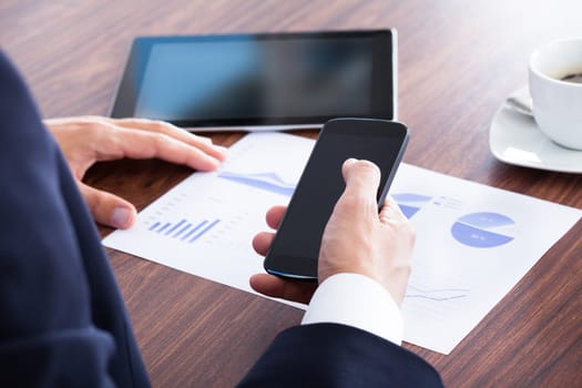 Businessman Holding Cell Phone And Analyzing Graph In Office