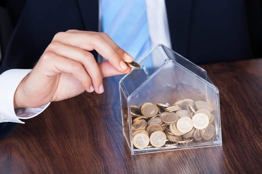 Close-up Of Businessman Inserting Euro Coin In Money Box