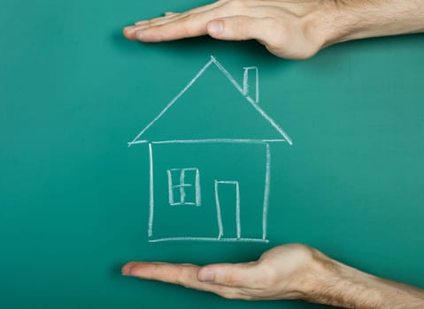Hand holding chalk drawing house on blackboard