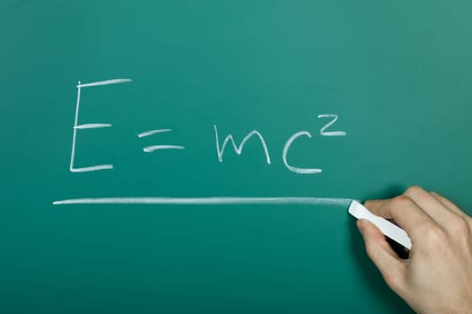 Hand writing relativity formula on green blackboard